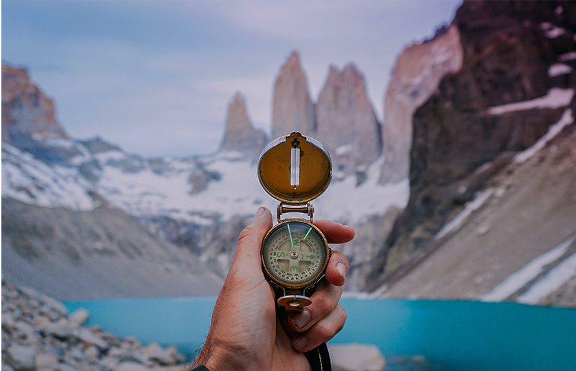 A person holding a compass on his hand facing a lake in a rocky mountains. The title placed on the photo writing: Listening to Your Gut